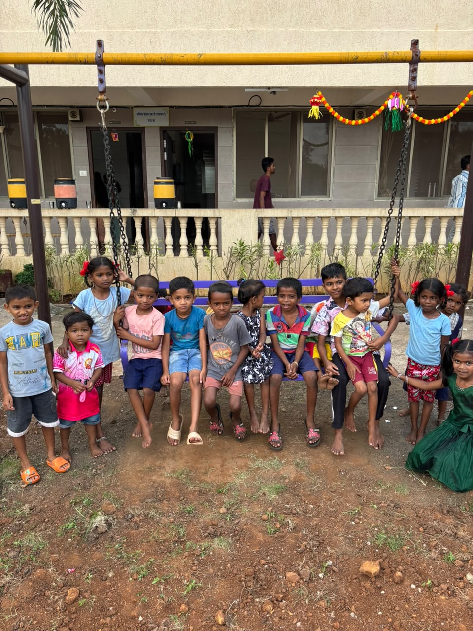 Children on a garden swing at the trust’s children’s home, with the campus building decorated for a festival behind them