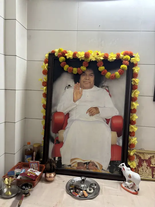A garlanded framed portrait with flowers, lamps and offerings placed before it at a shrine