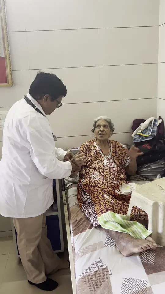 A doctor in a white coat attending to an elderly woman sitting on her bed