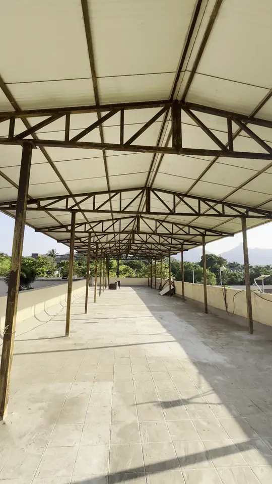 A long covered terrace with a steel roof frame, open to the fields and hills beyond